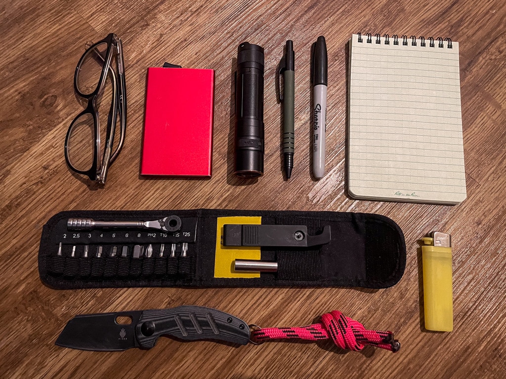 A layout of some common EDC items, including a pocket knife, lighter, torch, and waterproof notepad.